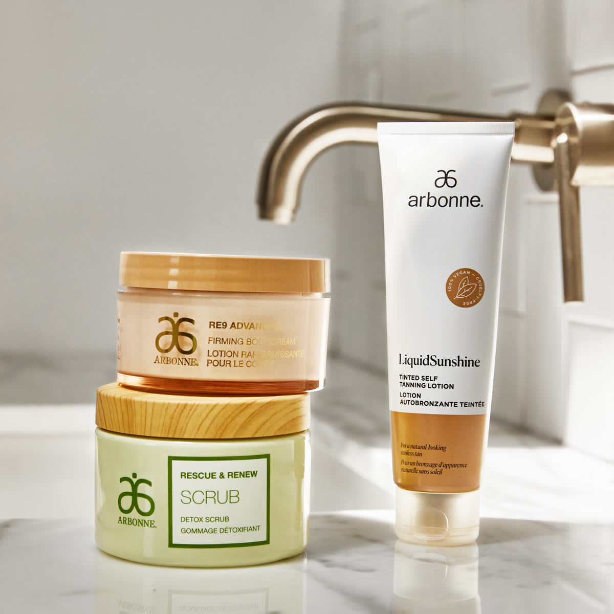 Arbonne scrub and body lotion stacked on a marble bathroom sink
